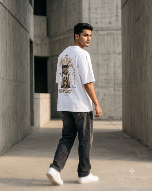 A man wearing a white graphic t-shirt with a large vintage-style print on the back, paired with dark gray jeans and white sneakers, walking through a concrete corridor.